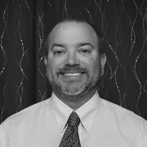 A black and white image of Jason Gerhard, a Principal at Integrity Federal Services. He is wearing a tie and smiling.